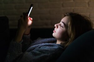 Young beautiful woman using smart phone at night in bed